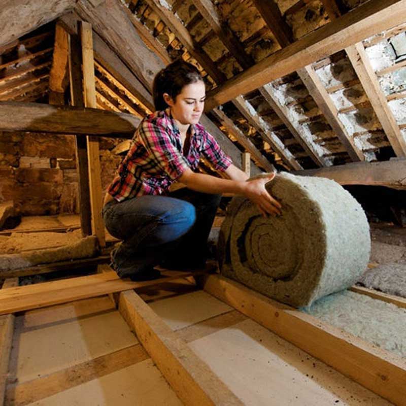 A woman fitting loft insulation roll in a roof 