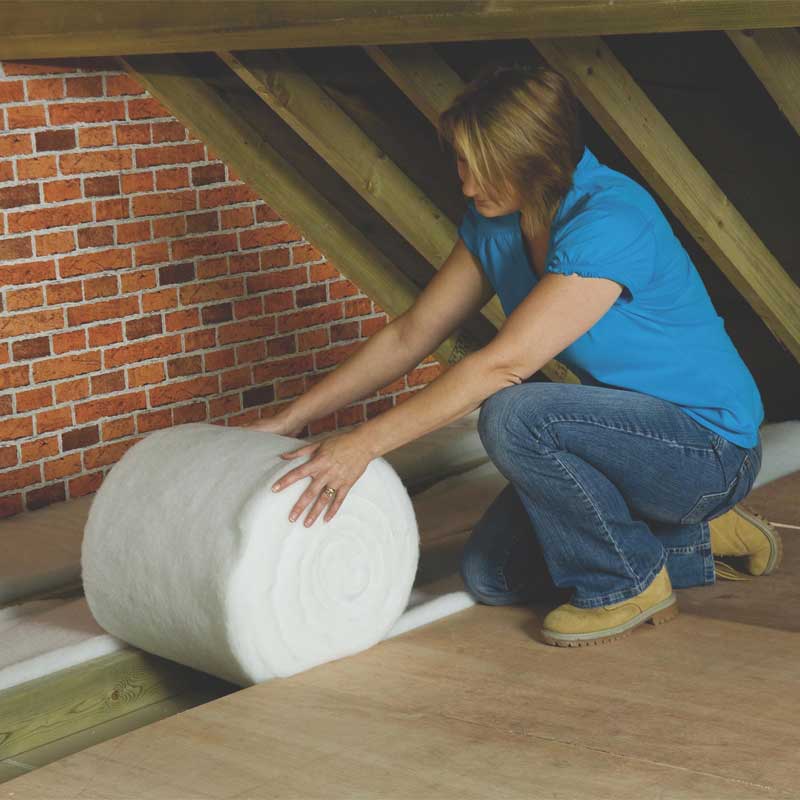 A woman laying loft roll insulation in her roof space