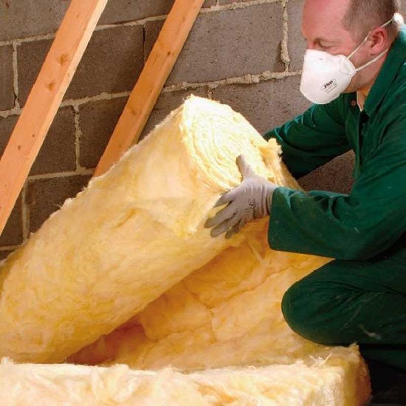 Man fitting glass wool insulation in a loft.