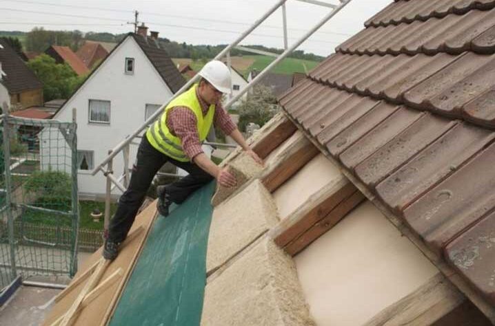 A tradesperson fitting external insulation on a pitched roof.