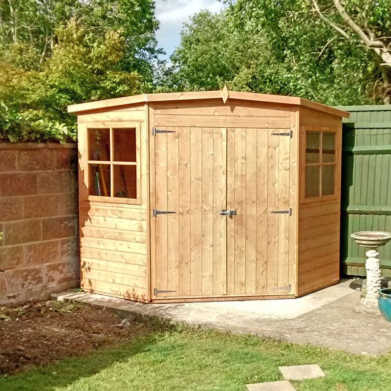 Corner shed in a garden with grass and a green fence behind it