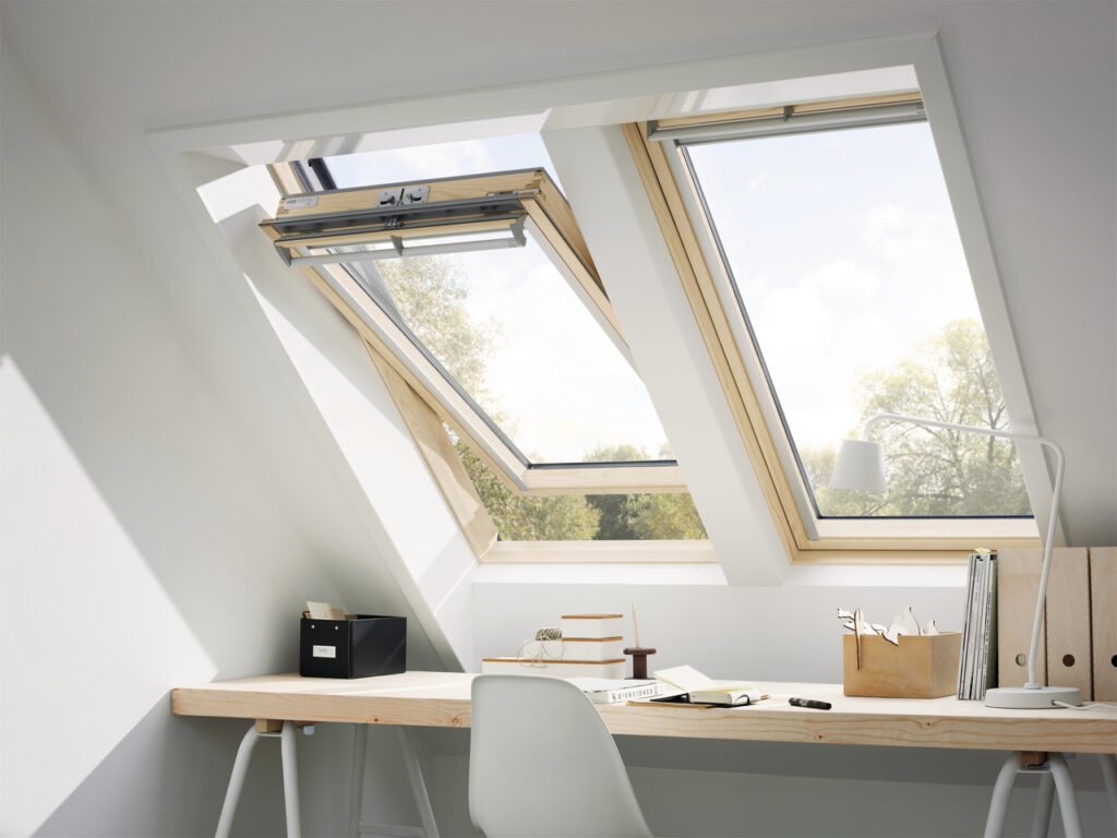 Two pitched roof windows, side by side in a bright and airy loft space which is being used as a home office. There is a desk with folders and stationary organisers facing the windows